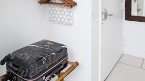 A hotel room with a neatly organized shelf holding folded towels and a hanging garment bag.