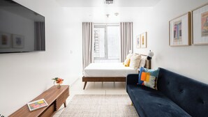 A modern bedroom with a bed, a blue sofa, a wooden bench, and a TV on the wall.