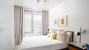 A bedroom with a large bed, a nightstand, a desk, and a window with curtains. - Manhattan loft Studio located Midtown NYC! #303 (New York)