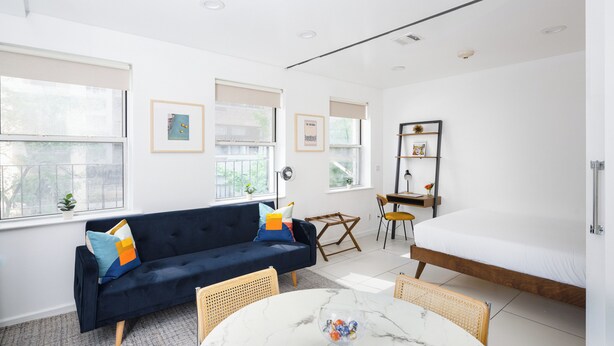 A modern, well-lit room with a dark blue sofa, a white bed, and a marble table. - Beautiful 2 beds Apt in Midtown NYC #301 (New York)