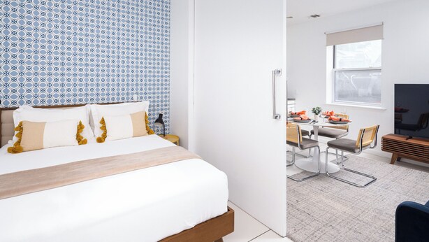 A modern hotel room with a large bed, a dining area with a table and chairs, and a TV.