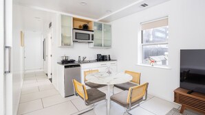 A modern kitchen with a microwave, stove, and cabinets. There is a dining table with four chairs and a TV in the corner.