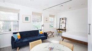 A modern, well-lit room with a dark blue sofa, a white bed, and a marble table.