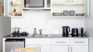 A modern kitchen with white cabinets, a black countertop, a microwave, a kettle, a toaster, and a dishwasher.