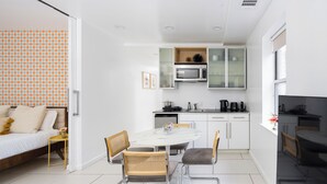 A modern kitchen with white cabinets, a microwave, and a dining area with a white table and chairs.