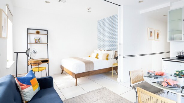 A modern, well-lit room with a bed, a desk, and a dining area. - Beautiful 2 beds Apt in Midtown NYC #201 (New York)