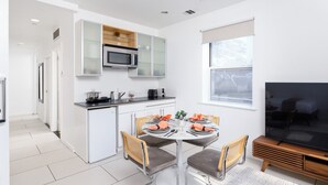 A modern kitchen with white cabinetry, a microwave, and a dining area with a table set for four. - Beautiful 2 beds Apt in Midtown NYC #201 (New York)