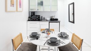 Moderni keittiö, jossa on valkoiset kaapit, mikroaaltouuni ja kahvinkeitin. Keittiössä on ruokapöytä, jossa on neljä tuolia, sekä maljakko täynnä kukkia.