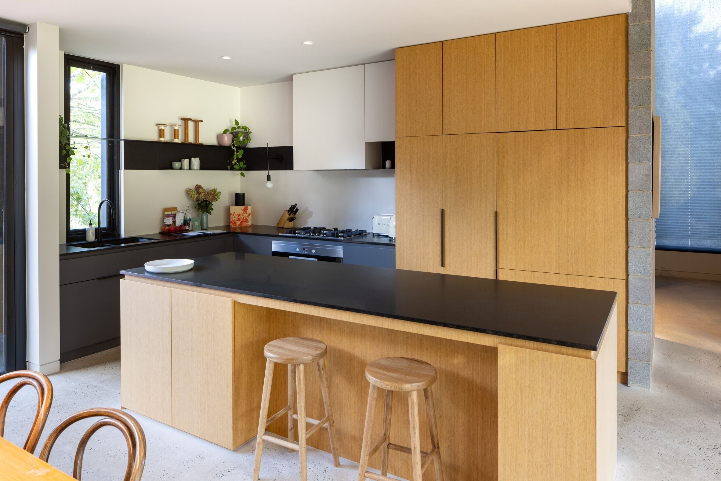 Een moderne keuken met houten kastjes, een zwart aanrecht en twee houten barkrukken.