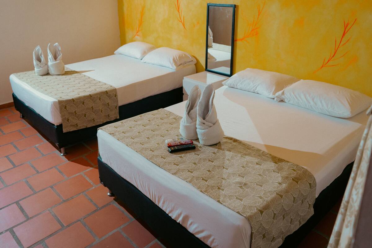 Two single beds with white linens, a mirror, and a pair of slippers on each bed.