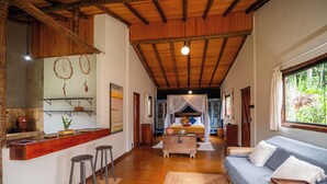 Een ruime kamer met een houten plafond, een bed met hemel, een sofa, een klein tafeltje en een bar met krukken.
