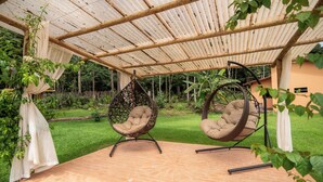 Een overdekt terras met twee hangstoelen en een vloer van baksteen.