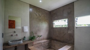 Een badkamer met een stenen wastafel, een spiegel, een handdoek, een raam en een bad.