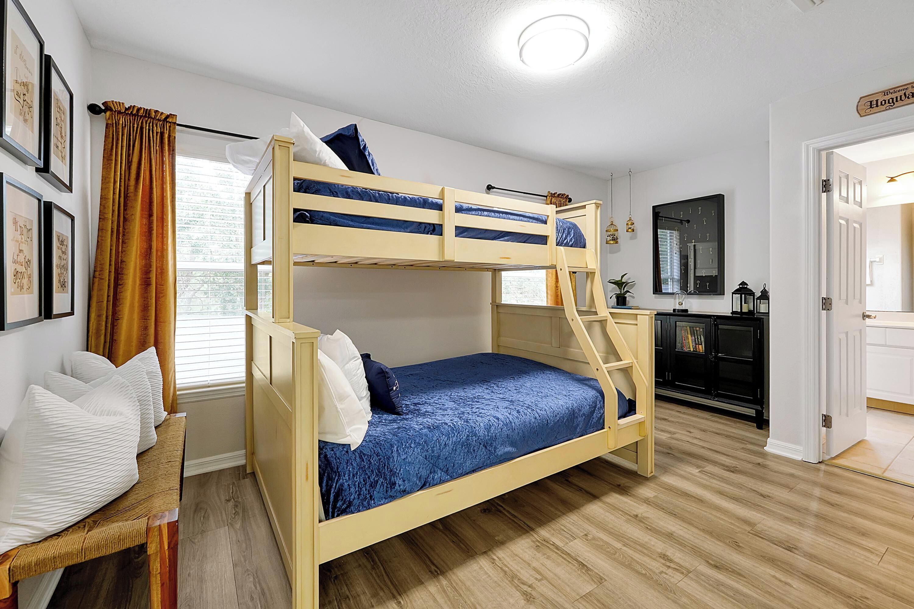 A bunk bed room with a desk, a mirror, and a door leading to another room.