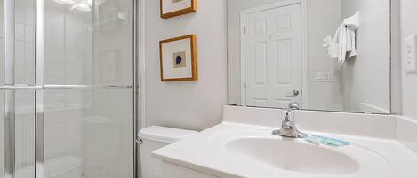 Une salle de bain avec une douche à parois de verre, des toilettes blanches, un lavabo avec un miroir et deux tableaux encadrés au mur.