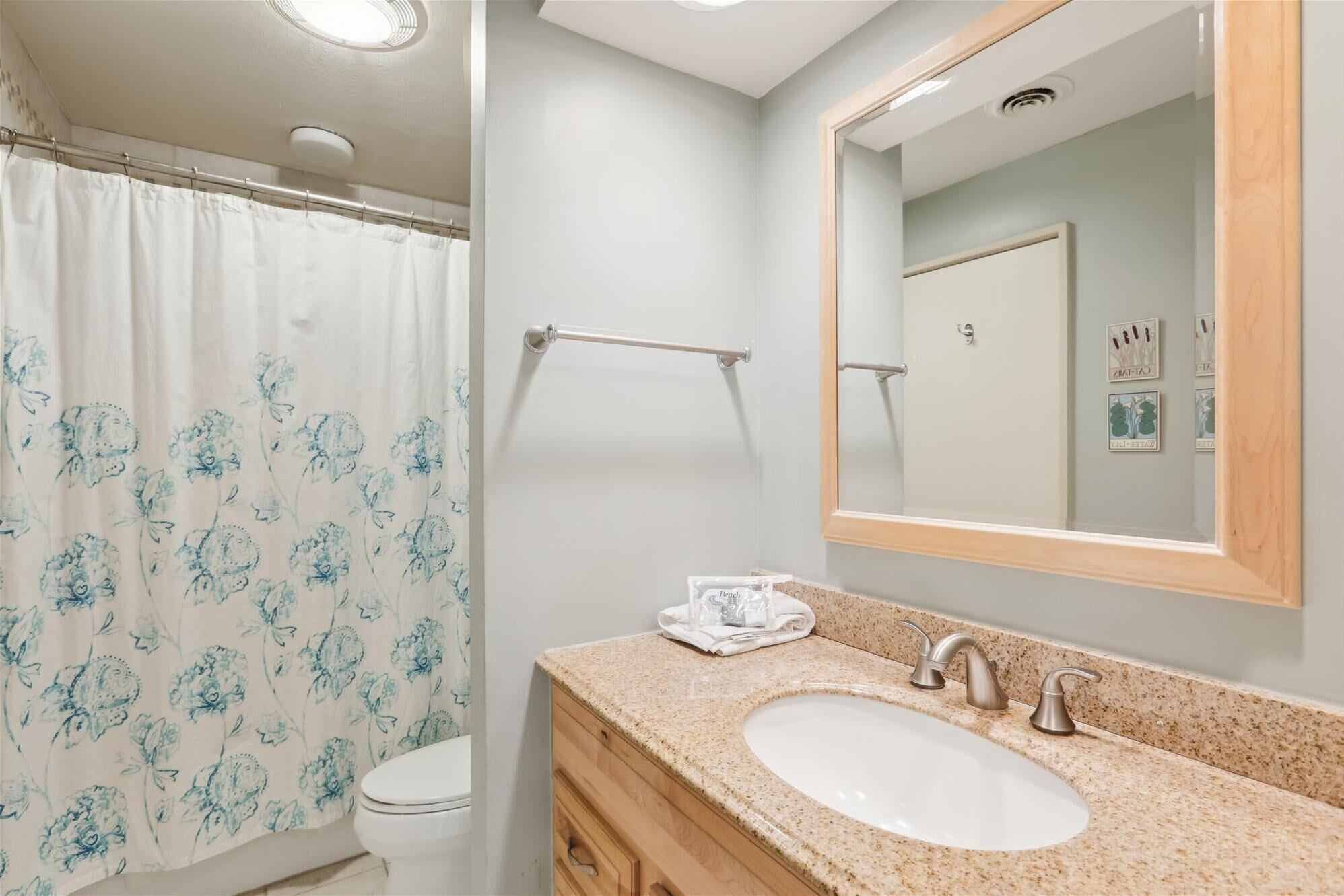 A bathroom with a shower curtain, a sink, a mirror, and a towel rack.