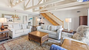A spacious living room with a high ceiling, a staircase, and a view of the kitchen.