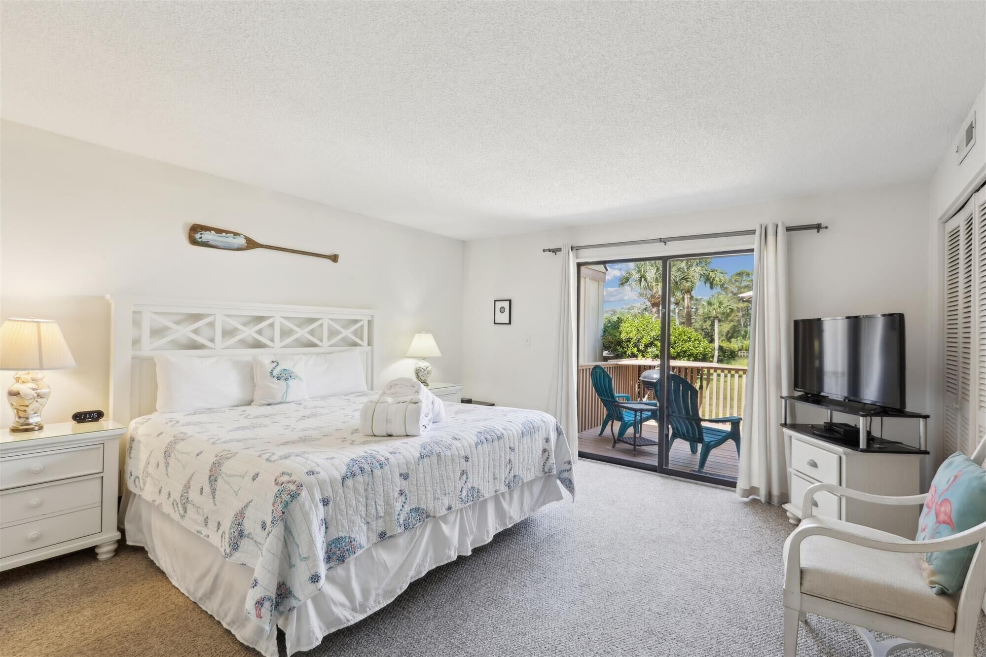 A bedroom with a bed, a nightstand, a TV, and a balcony with outdoor furniture.