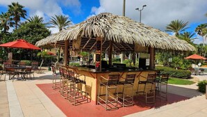 An outdoor bar area with a thatched roof, bar stools, and red umbrellas. - Cozy Retreat 4BR-walk to Resort's Lazy River,pools-12 miles to Walt Disney World (Davenport)