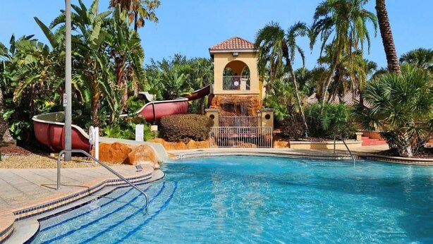 A swimming pool with a tiled deck, palm trees, and a small building with a red roof. - Cozy Retreat 4BR-walk to Resort's Lazy River,pools-12 miles to Walt Disney World (Davenport)