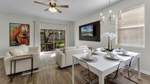 A modern living room with a white sofa, dining table set for four, and a ceiling fan. - Cozy Retreat 4BR-walk to Resort's Lazy River,pools-12 miles to Walt Disney World (Davenport)