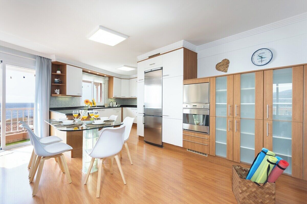 A modern kitchen with white cabinets, stainless steel appliances, and a dining area with white chairs.