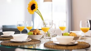 En frukostuppdukning med ett glasbord, tallrikar, skålar, croissanter, en kanna med apelsinjuice och en solros.
