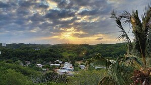 Un paysage comprenant un coucher de soleil, une végétation luxuriante et des bâtiments dispersés.