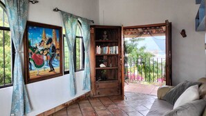 Un salon avec un sol carrelé, un canapé, une bibliothèque et un tableau représentant une scène culturelle.