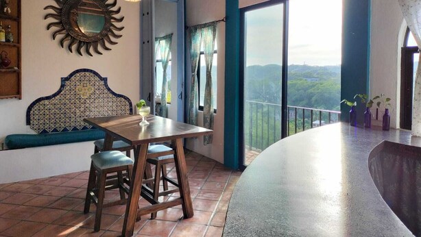 Un coin repas avec une table et des chaises en bois, un miroir décoratif et une vue sur l’extérieur.