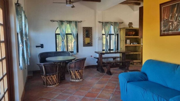 A room with a round table, two chairs, a blue sofa, and a wooden bookshelf. - Casa Pajaros - Balcony (La Cruz de Huanacaxtle)