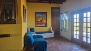 A room with a yellow wall, a blue sofa with cushions, a painting, and a door with windows. - Casa Pajaros - Balcony (La Cruz de Huanacaxtle)