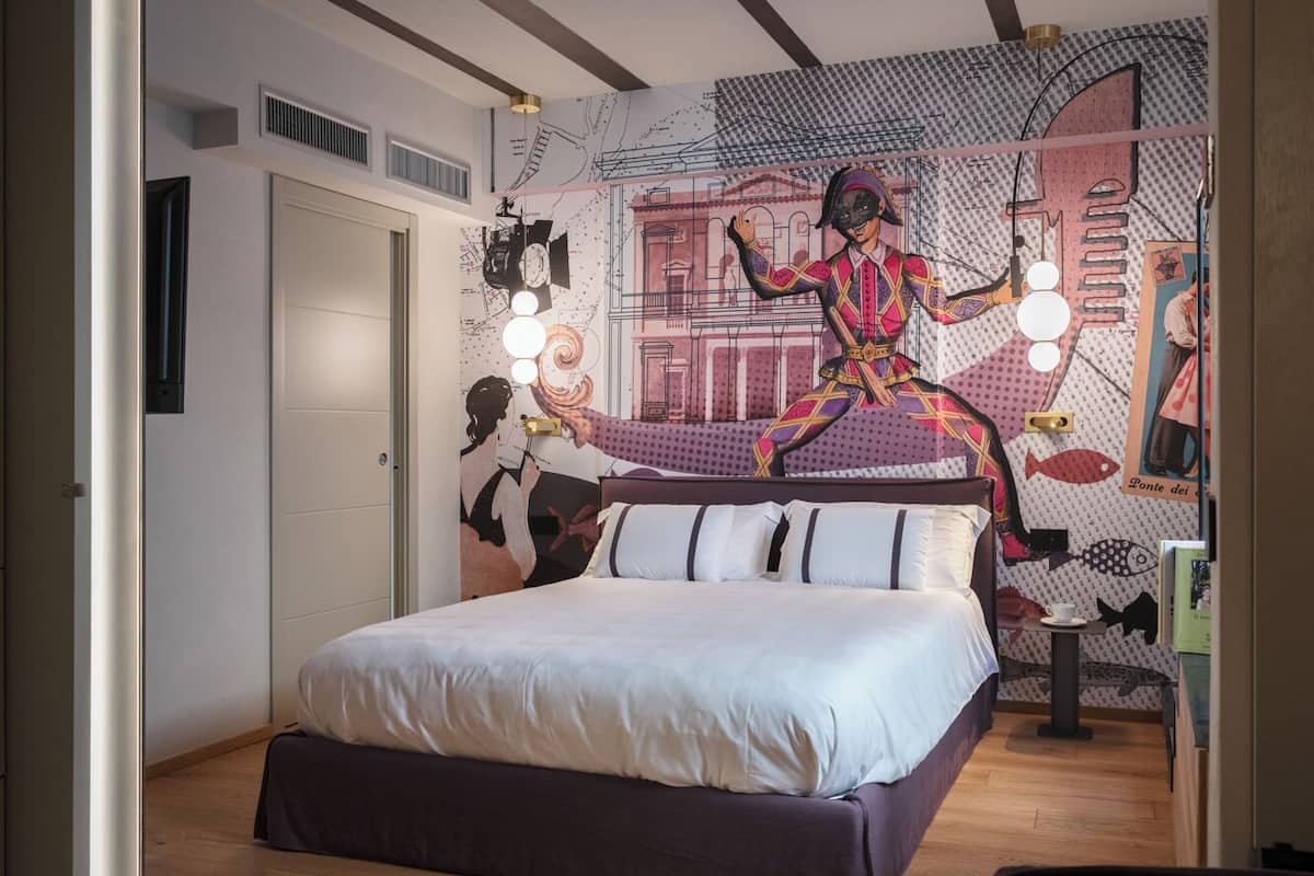 A bedroom with a bed, a wall mural, and a small table with a cup.