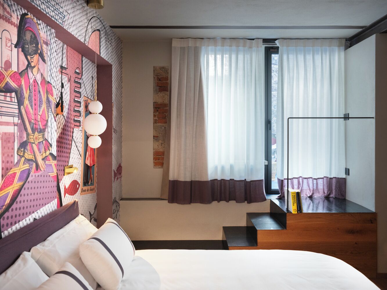 Quarto de hotel moderno com uma cama grande, uma mesa com cadeira, uma janela com cortinas e uma parede com um mural colorido.