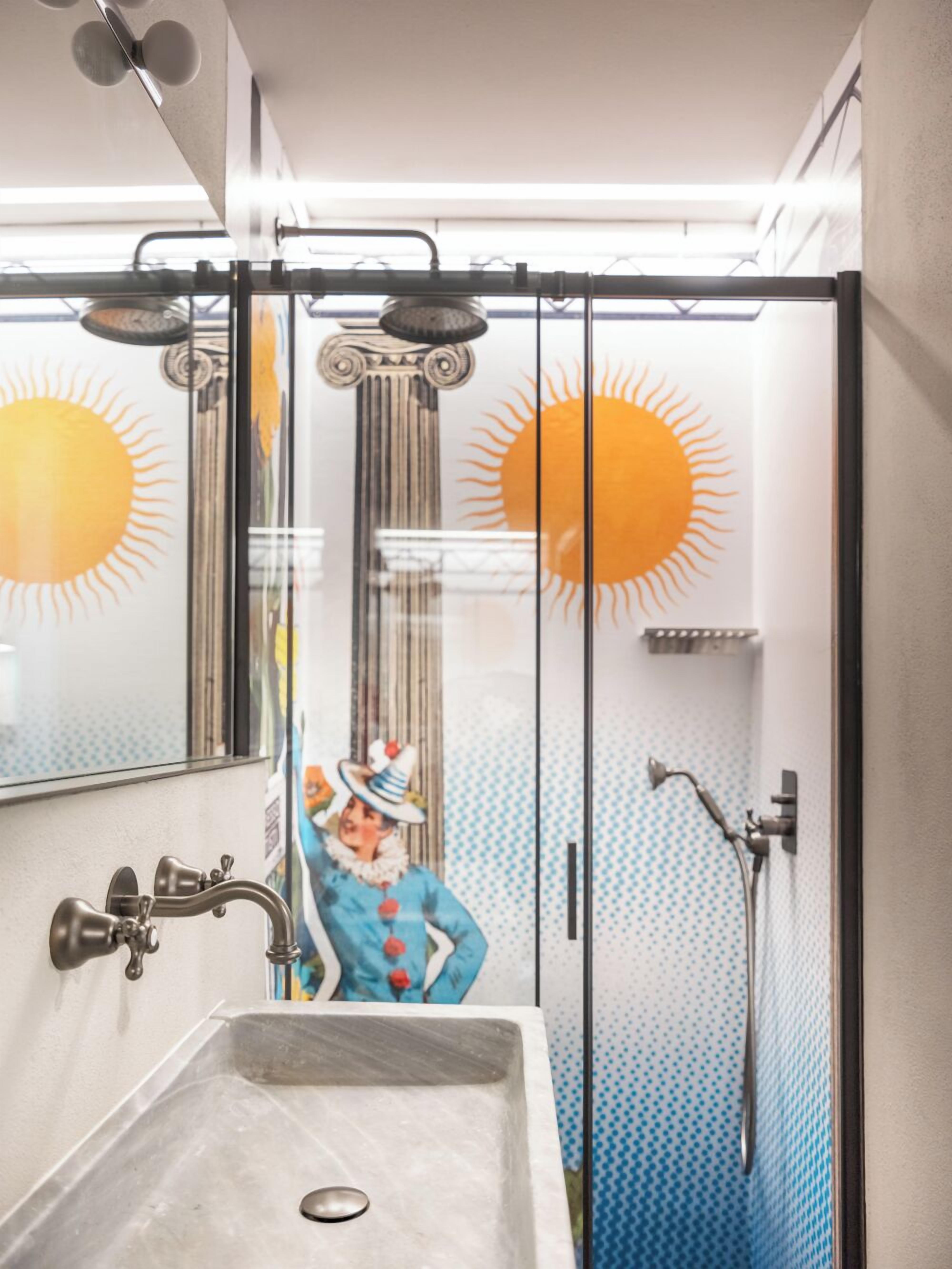 Une salle de bain dotée d’une douche à parois de verre, d’un lavabo avec un robinet moderne et d’un motif décoratif en forme de soleil sur les murs.