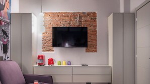 A modern living room with a brick accent wall, a flat-screen TV mounted above a white console table, a purple sofa, and a coffee maker. - Pietrasanta Ai Teatri (Pietrasanta)