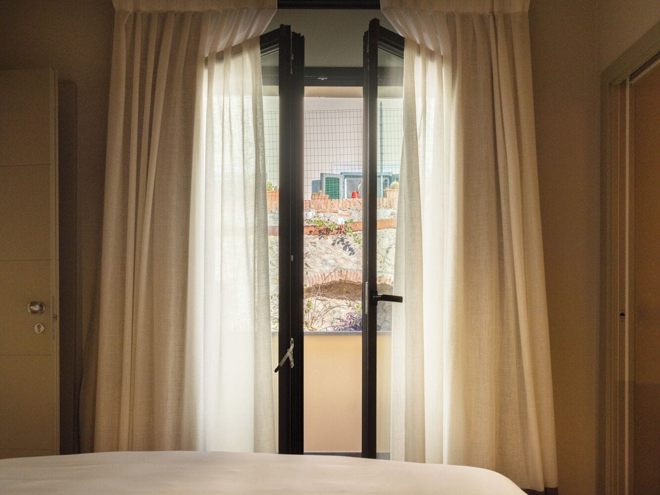 Quarto de hotel com cama, porta com vista para o exterior e janela com cortinas.