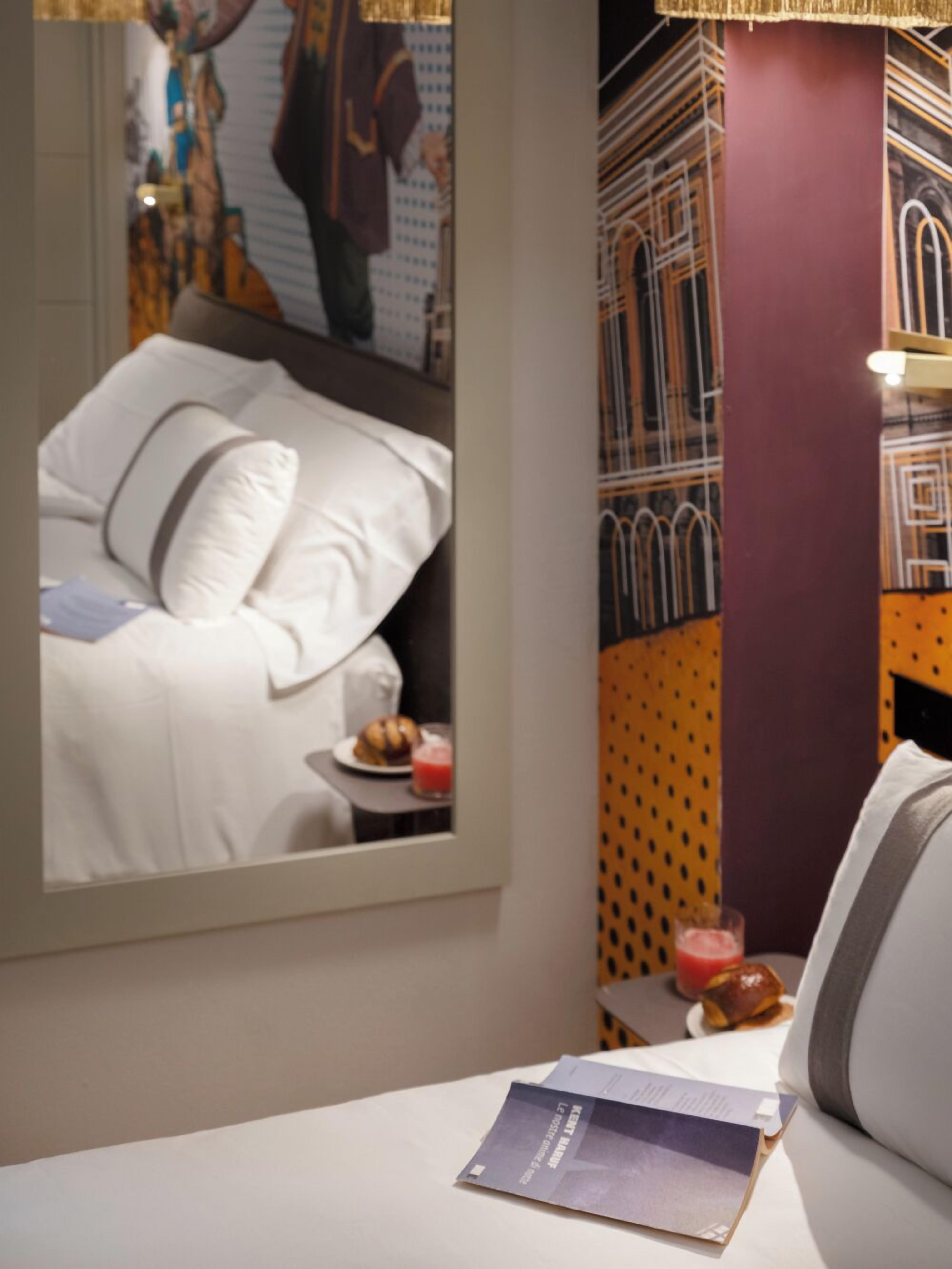 A hotel room with a bed, a nightstand with a book, a glass of juice, and a candle.
