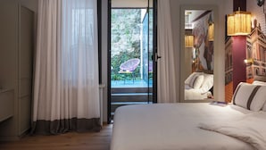 A hotel room with a bed, a window with curtains, a balcony with a chair, and a wall with a mural. - Pietrasanta Ai Teatri (Pietrasanta)