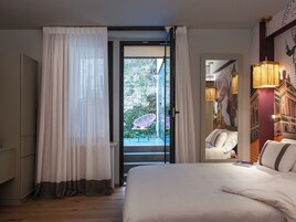 A hotel room with a bed, a window with curtains, a balcony with a chair, and a wall with a mural.