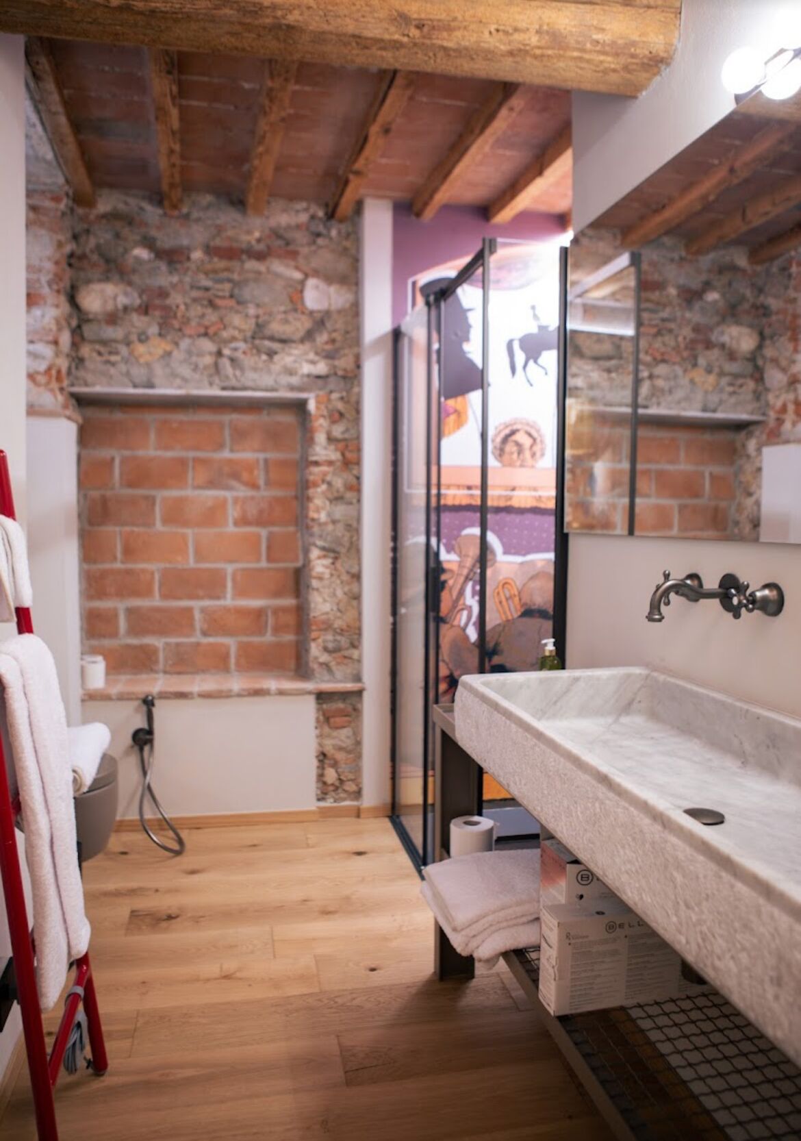 Ein Badezimmer mit Steinwand, Holzboden, einem weißen Waschbecken, einem Spiegel und einer Duschkabine.