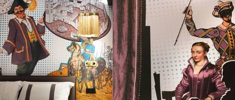 A room with a bed, a mural of historical figures, and a sign that reads "PROVE IN CORSO!".