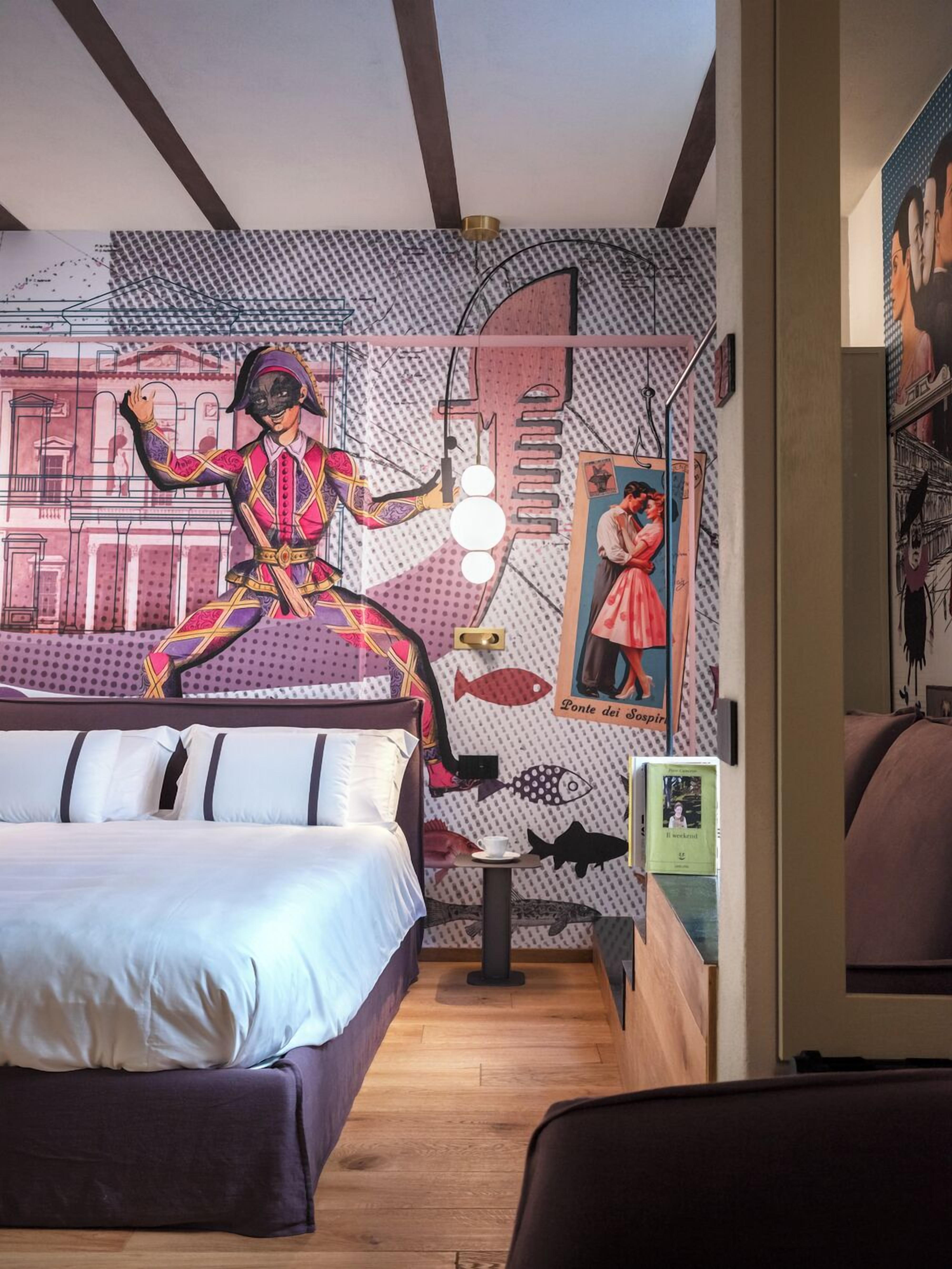 A hotel room with a bed, a small table, and a wall decorated with various artworks and a mural.