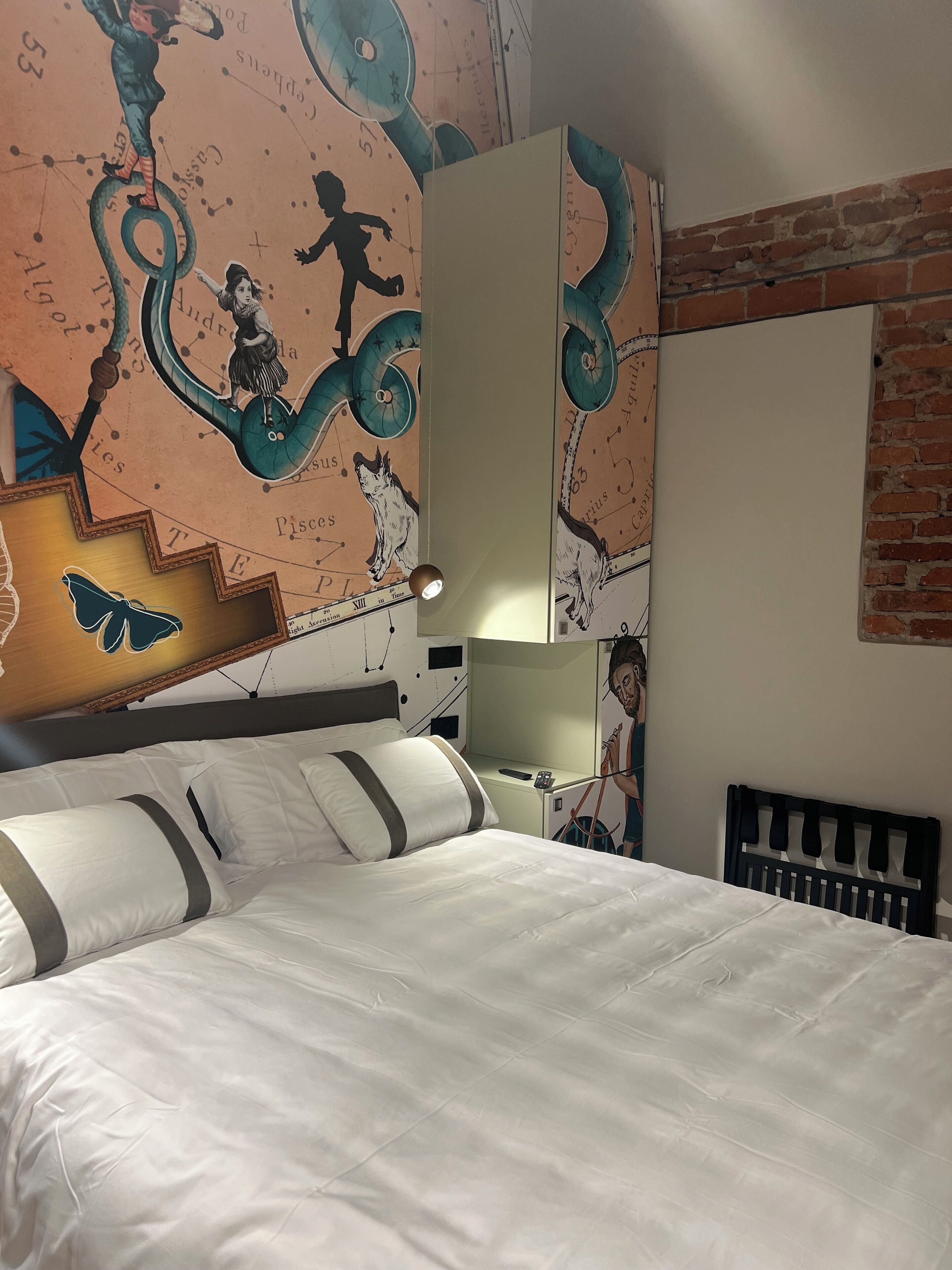 Ein Hotelzimmer mit einem großen Bett, einer Backsteinwand und einem Wandgemälde mit Tierkreiszeichen und einer Zeichentrickfigur.