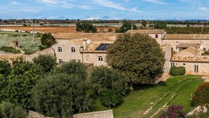 A stone building with multiple windows and a solar panel on the roof, surrounded by greenery and a clear sky. - Villa Ramunna 6, Emma Villas (Rosolini)