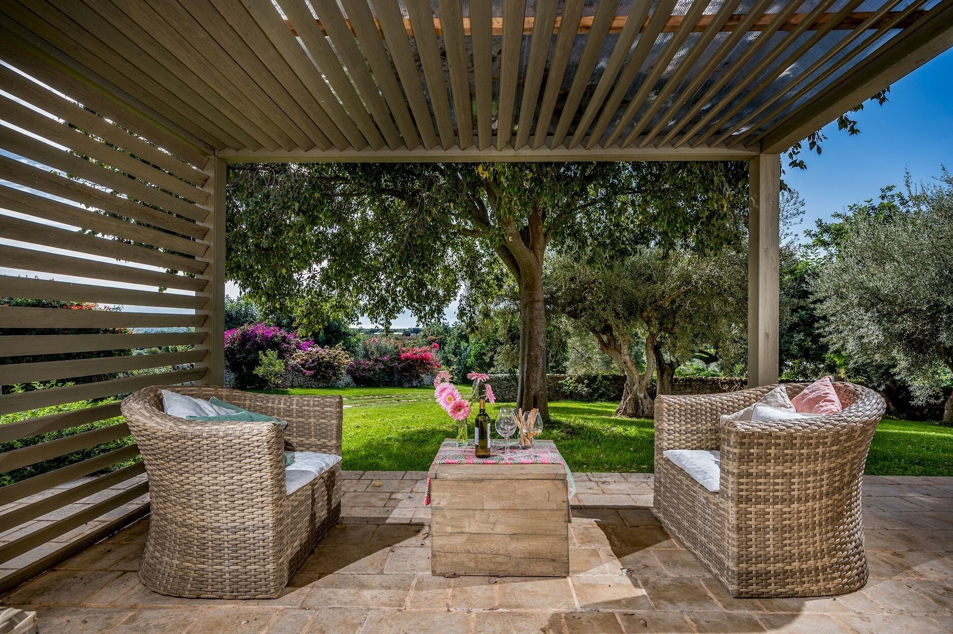 Ein Patio im Freien mit Korbmöbeln, einem Steintisch und einer Pergola darüber.
