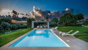 A swimming pool with lounge chairs and a pergola, surrounded by greenery and a stone wall. - Villa Ramunna 6, Emma Villas (Rosolini)
