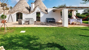 A rustic house with conical roofs, a patio area with outdoor furniture, and a well-maintained lawn.