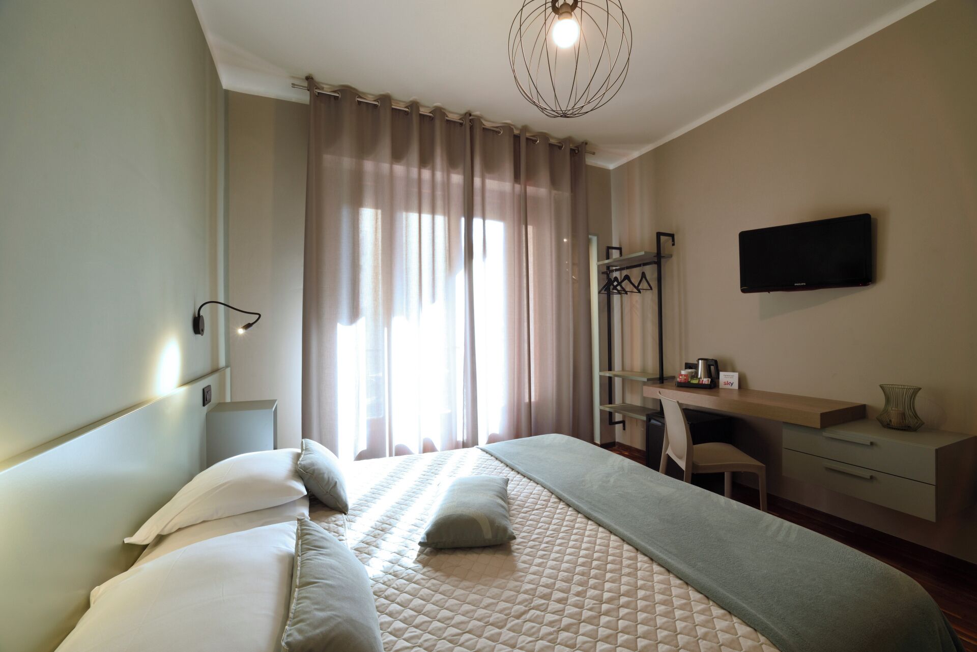 A hotel room with a bed, a desk, a chair, a television, and a window with curtains.