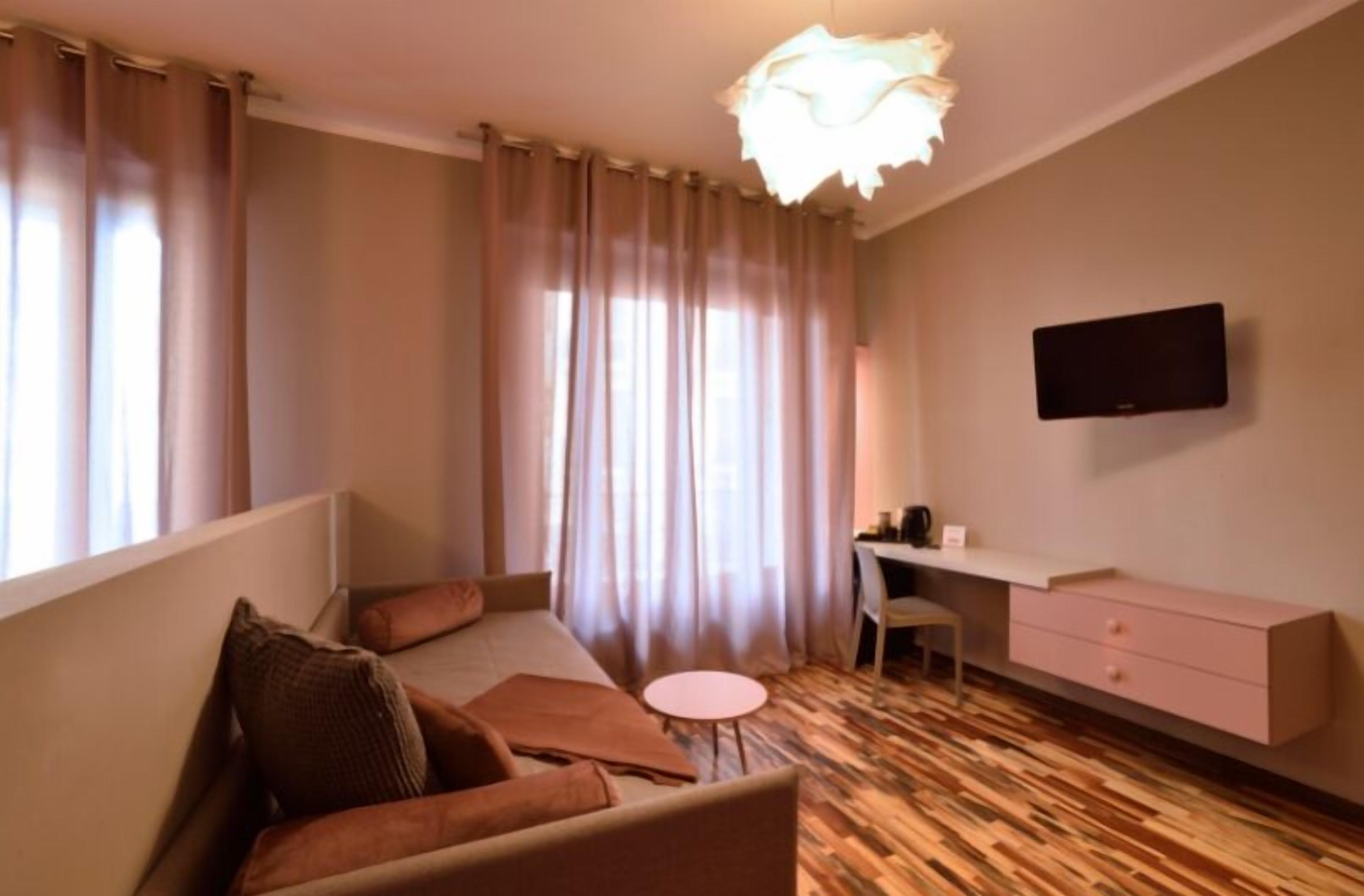 Habitación de hotel moderna con cama, escritorio, silla, una mesita y televisor en la pared.